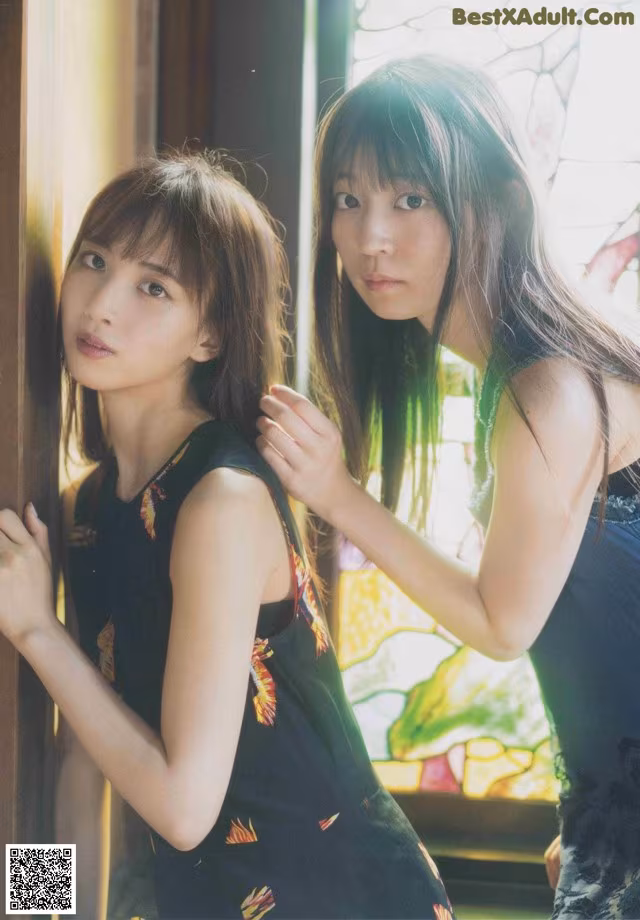 Two young women standing next to each other near a window.