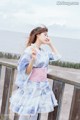 A woman in a blue and pink kimono standing on a wooden railing.