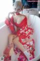 A woman in a red kimono sitting in a bathtub with a fan.