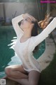 A woman in a white bodysuit sitting by a swimming pool.