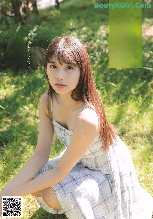 A woman in a plaid dress sitting on the grass.