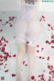 A woman in a white dress is surrounded by rose petals.