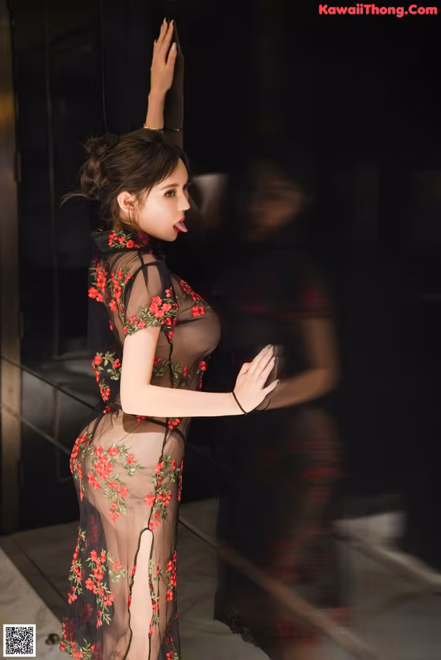 A woman in a sheer black dress with red flowers on it.
