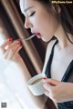 A woman in a black dress eating a cup of coffee.