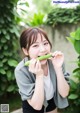 A young woman holding a cucumber in front of her mouth.