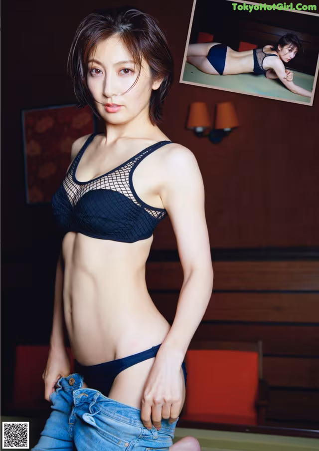 A woman in a black bra top and blue jeans posing for a picture.