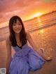 A woman in a blue dress sitting on the beach.