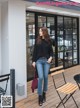 A woman is standing outside of a restaurant wearing a black sweater and jeans.