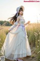 A woman in a white dress and hat standing in a field.